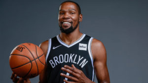 Kevin Durant holding a basketball and smiling because the Nets love NYC.