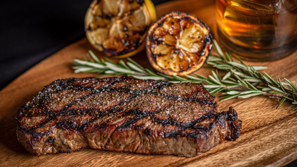 Photo of a seared steak with lemon and a glass of whiskey. One of the best foods to pair with Irish Whiskey.