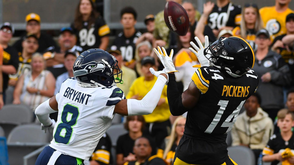 Photo of young steelers offense player George Pickens attempting to catch the ball while being blocked by a Seattle Seahawks player.